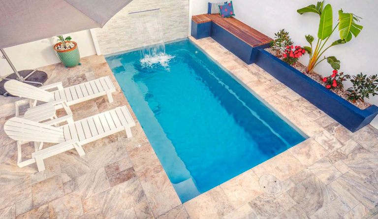 The Harmony 16 compact fiberglass pool in Silver Grey with flowering garden and coastal ocean backdrop