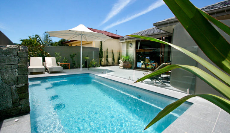 The Harmony 16 fiberglass pool in Silver Grey with pergola shade sail and tropical landscaping
