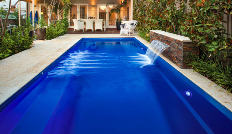 The Harmony 26 fiberglass pool in Sapphire Blue with water feature spillover and timber pool house