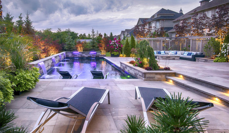 The Pinnacle fiberglass pool illuminated at dusk with LED lighting and splash deck lounge chairs in Graphite Gray