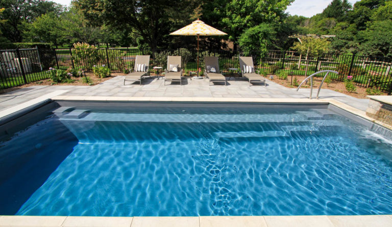 The Reflection fiberglass pool full length bench seat and swim channel with poolside lounge chairs in Graphite Grey