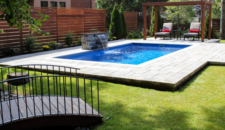 Leisure Pools Reflection fiberglass pool in Sapphire Blue with water feature and lush garden backdrop