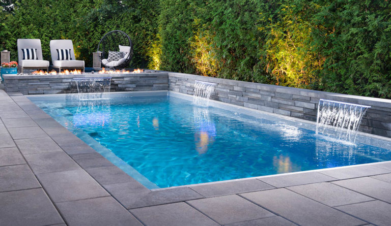 Leisure Pools Reflection fiberglass pool in Silver Grey with evening lighting and bamboo hedge backdrop