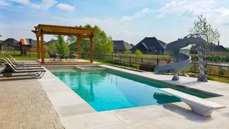 Leisure Pools Icon fiberglass pool in Diamond Sand with pergola and lounge chairs on splash deck