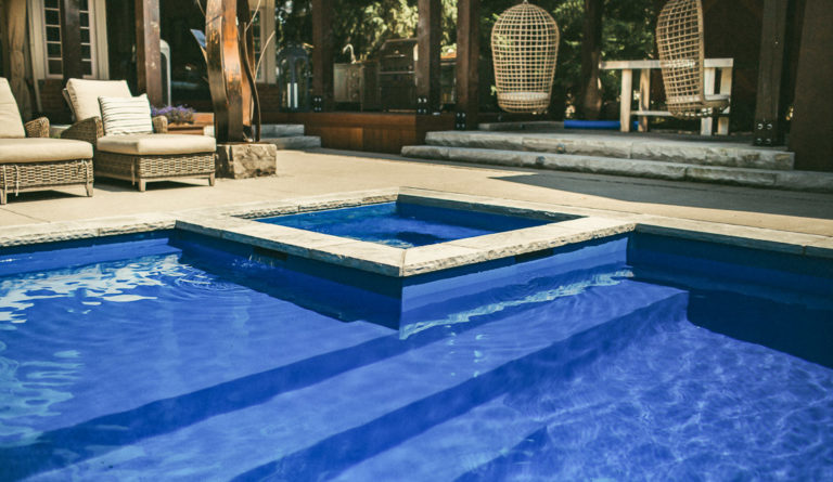The Icon fiberglass pool in Sapphire Blue with poolside lounge chairs and striped umbrellas