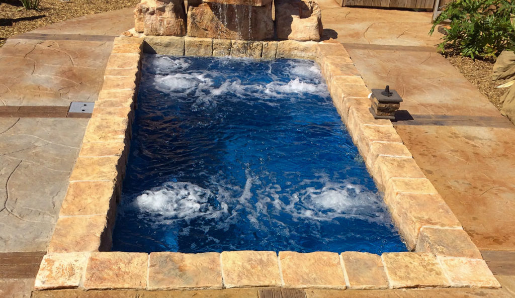 Leisure Pools Palladium Plunge fiberglass pool in Graphite Gray with rock waterfall and stone paver surround