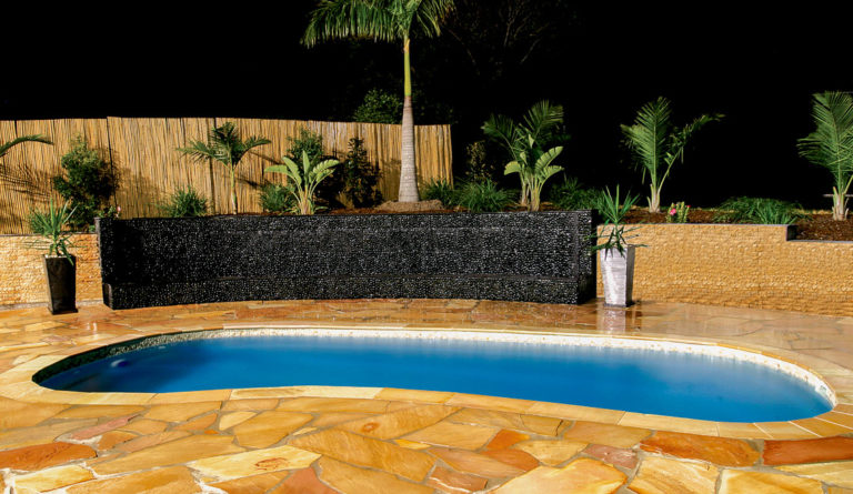 The Tuscany inground fiberglass pool with evening lighting and tropical landscaping