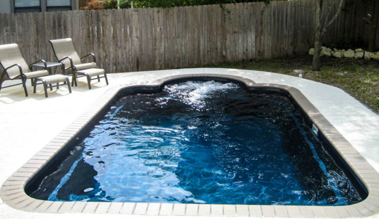 The Courtyard Roman fiberglass pool in Ebony Blue with fenced backyard and poolside lounger