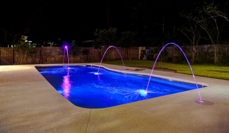 Leisure Pools Moroccan fiberglass pool illuminated at night with fountain jets in Sapphire Blue
