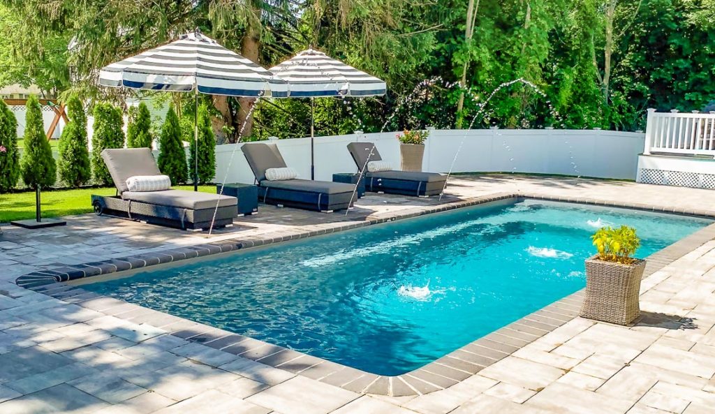 The Reflection with Splash Deck fiberglass pool in Graphite Grey with lounge chairs and tropical landscaping