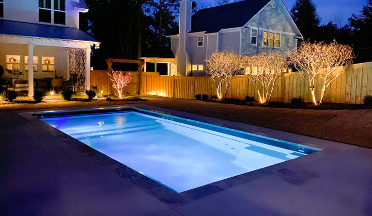 Leisure Pools Summit fiberglass pool illuminated at night with landscape lighting in Graphite Grey