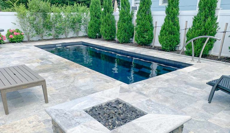 The Harmony 23 fiberglass pool in Ebony Blue with stone paver surround and poolside fire feature