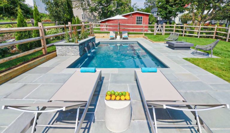 Leisure Pools Reflection fiberglass pool aerial view with poolside seating and red barn backdrop in Graphite Grey