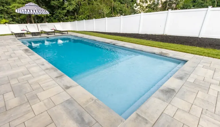 Leisure Pools Pinnacle fiberglass pool in Silver Grey with open backyard and white vinyl fence