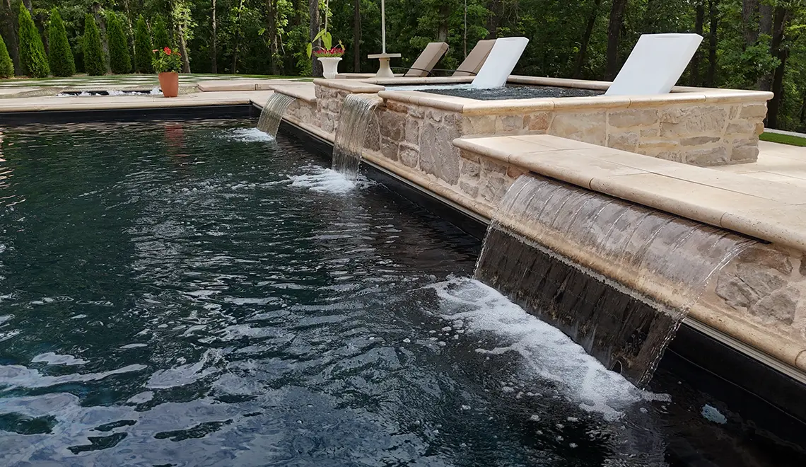 Leisure Pools Wave fiberglass pool with raised spa and lounge chairs on tanning ledge