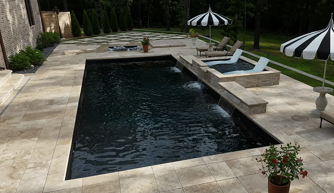Leisure Pools Wave fiberglass pool with raised spa and lounge chairs on tanning ledge