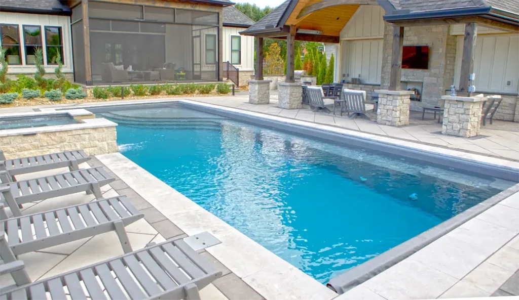Leisure Pools Wave fiberglass pool with pool house and stone paver surround