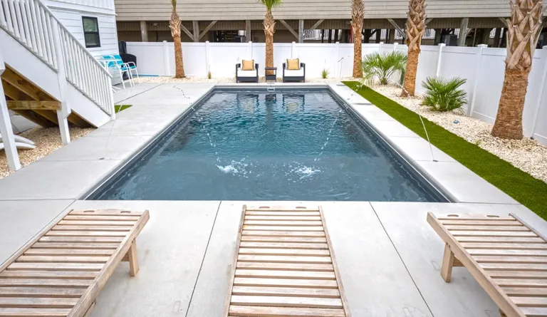 The Summit fiberglass pool full-width splash deck head-on view with palm trees in Graphite Grey