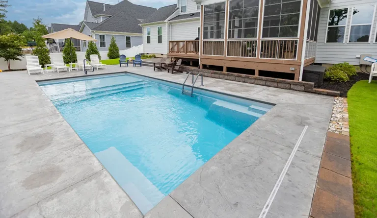 Leisure Pools Pinnacle fiberglass pool with screened porch and white fence backdrop