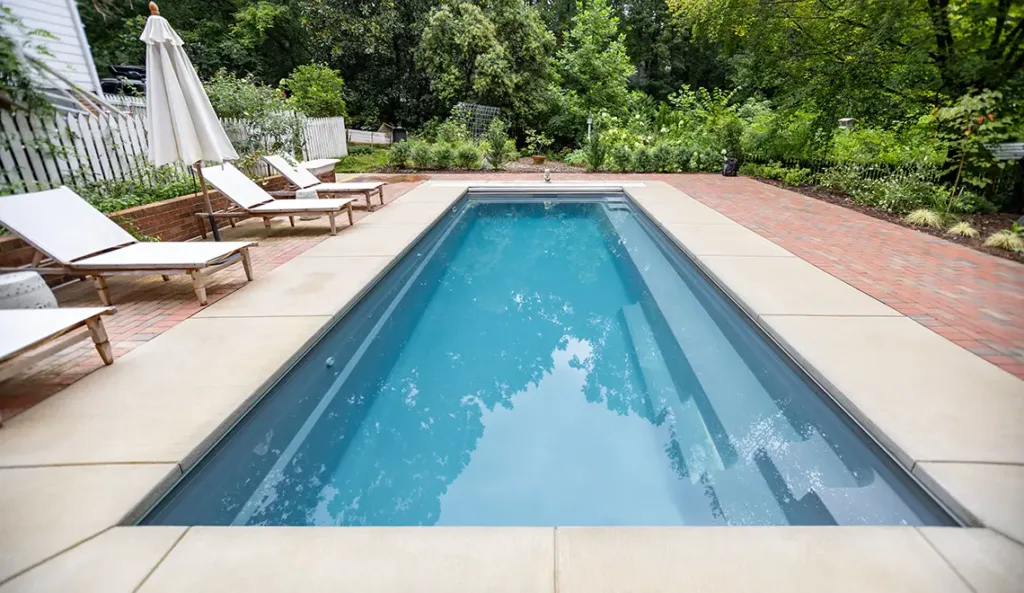 Leisure Pools Reflection fiberglass pool in Graphite Grey with poolside lounge chairs and open backyard