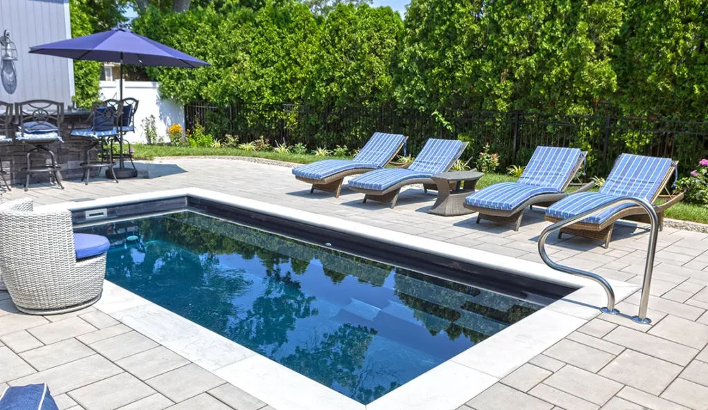 Leisure Pools Harmony 20 fiberglass pool in Ebony Blue with poolside lounge chairs and patio