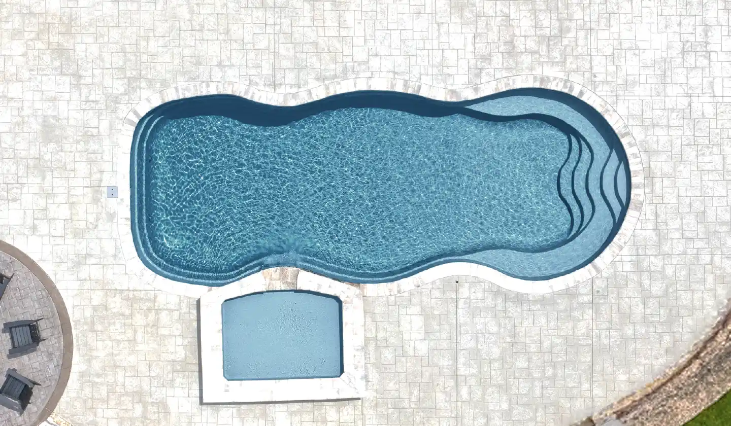 The Caribbean™ fiberglass pool in Graphite Grey, featuring wraparound seating and a long open swimming space.