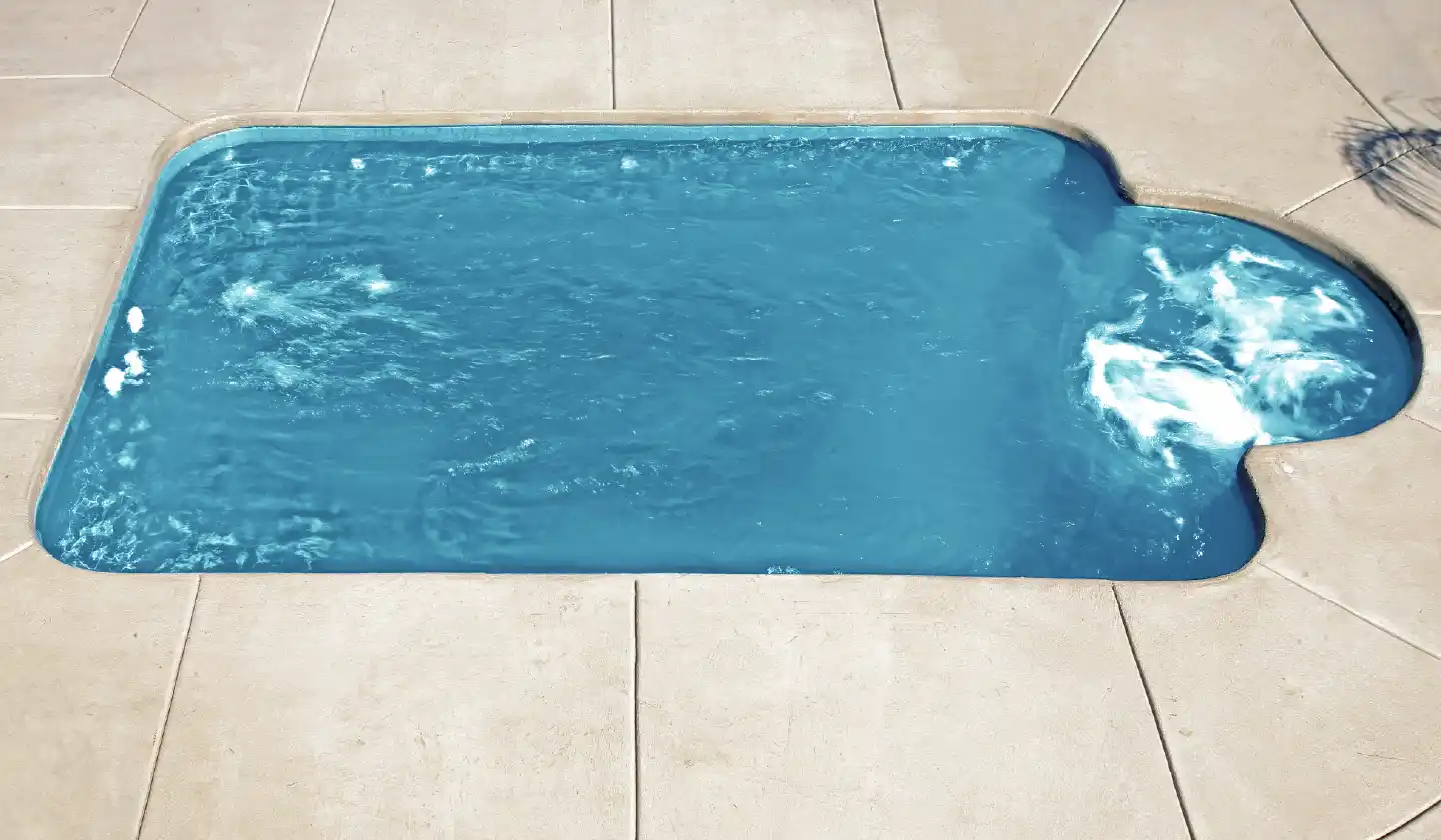 The Courtyard Roman™ fiberglass pool in Aquamarine, featuring a compact keyhole shape and rounded seating nook.