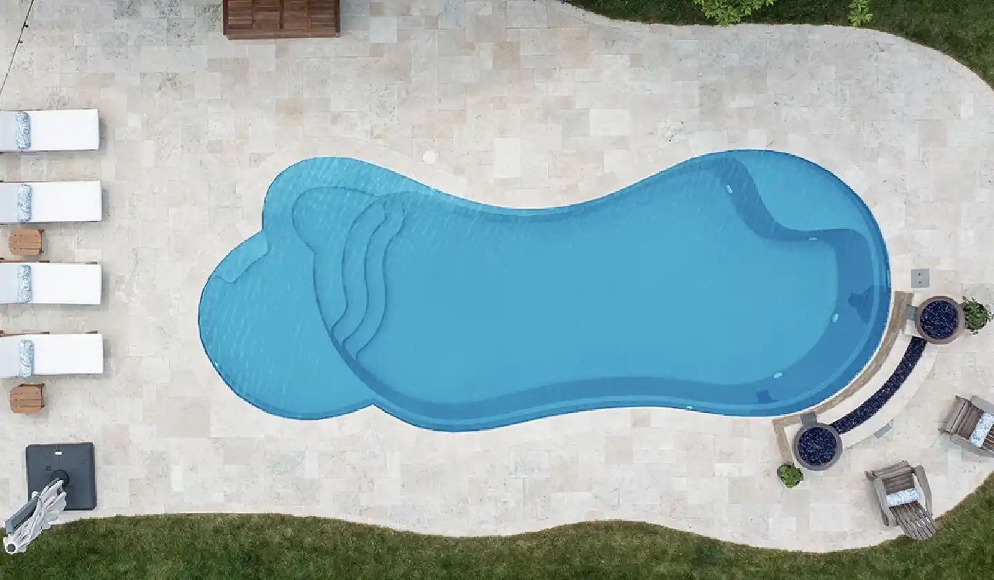 The Eclipse™ fiberglass pool in Crystal Blue, with flowing pool edges and a shallow lounging shelf at one end.