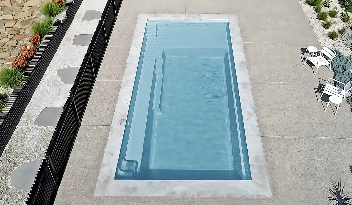 The Elite™ fiberglass pool in Shimmer Sky, featuring straight pool edges, submerged seating and a shallow lounging deck.