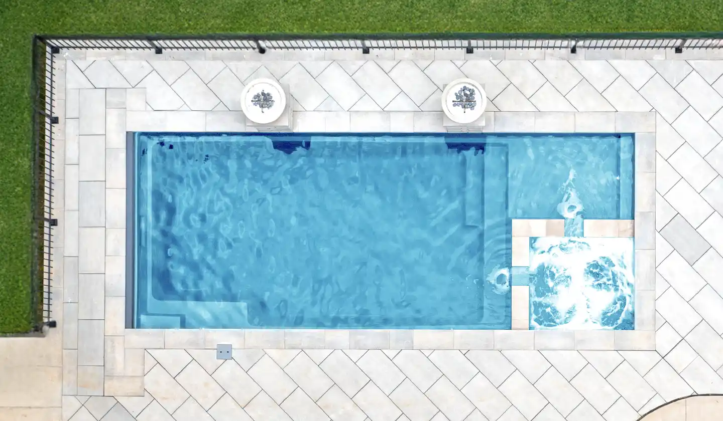 The Limitless™ fiberglass pool in Crystal Blue, with a built-in square spa beside the shallow lounging deck.