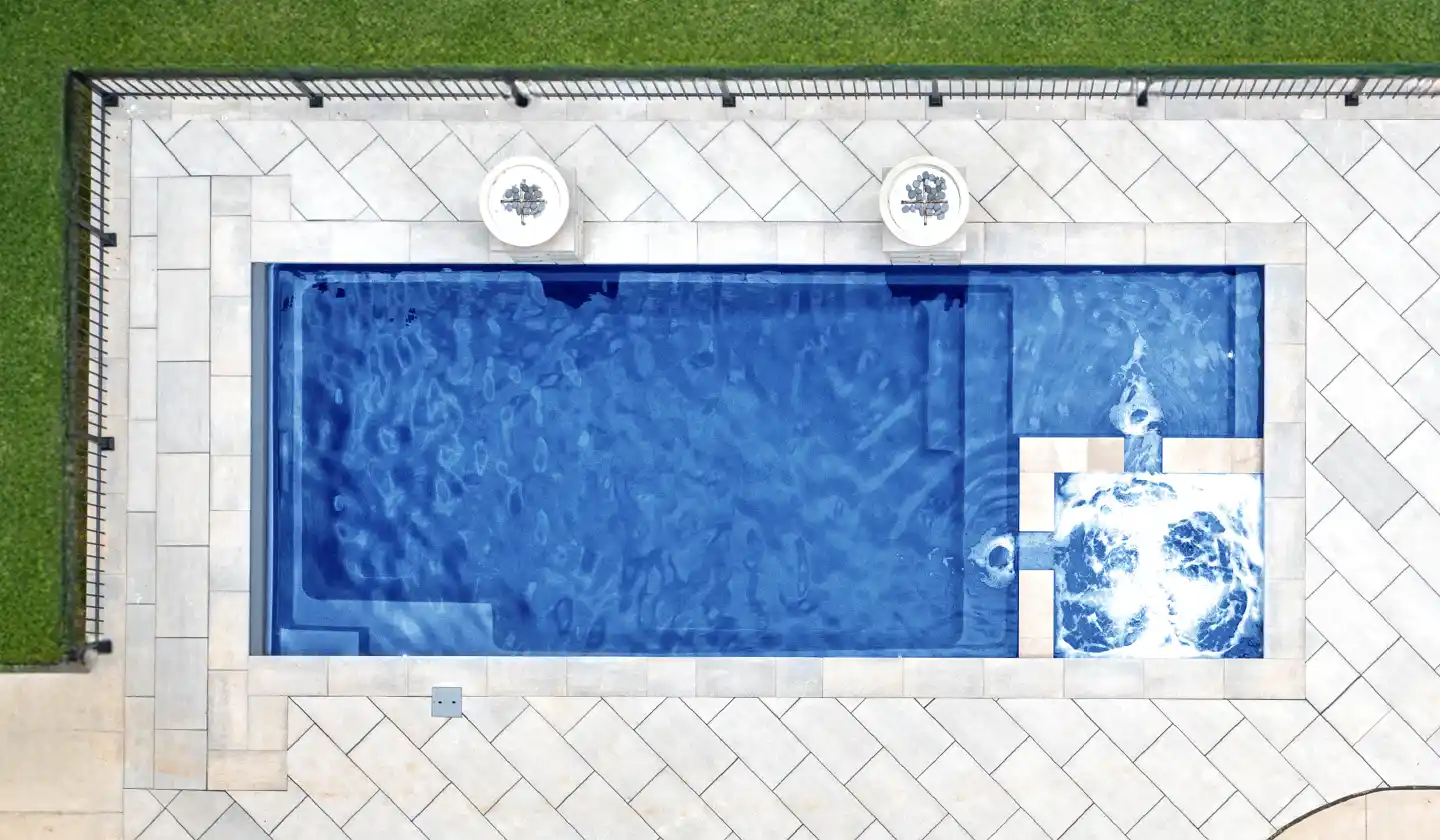 Overhead view of The Limitless™ fiberglass pool in Sapphire Blue, with an integrated spa and splash deck surrounded by pale paving.