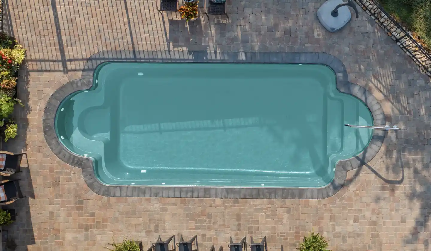 The Roman™ fiberglass pool in Diamond Sand, with an open swim space framed by rounded ends and stone paving.