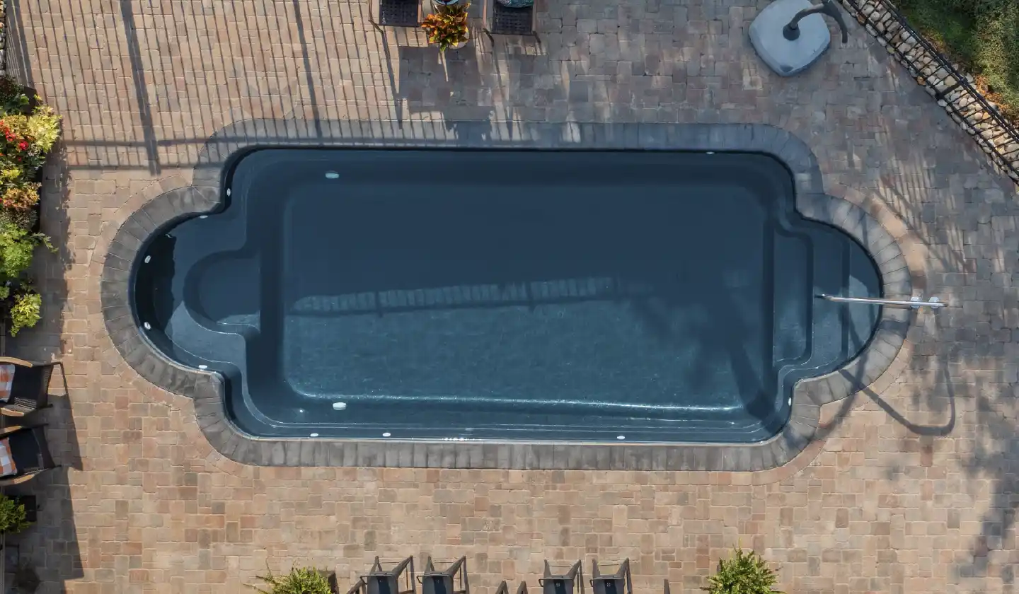 The Roman™ in Graphite Grey, a fiberglass pool with stepped entry and rounded seating alcoves around the swim area.